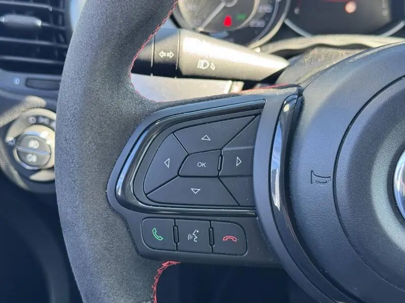 Gros plan sur le volant cuir sport de la Fiat 500X 2024, avec commandes multifonctions et surpiqûres rouges visibles.