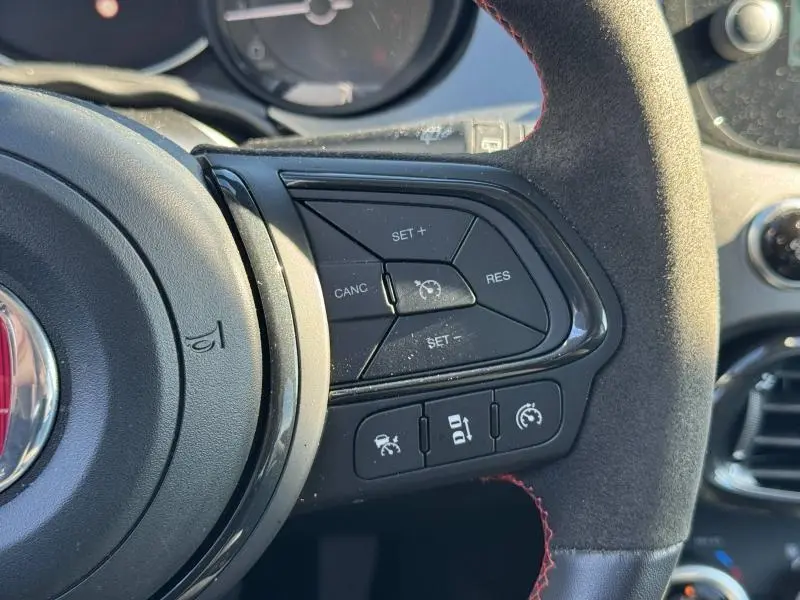 Gros plan sur les commandes de régulateur de vitesse au volant cuir noir avec surpiqûres rouges du Fiat 500X rouge Passione pastel.