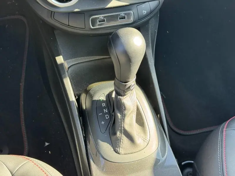 Gros plan sur le levier de vitesses automatique noir de la FIAT 500X rouge Passione pastel, avec coutures rouges visibles.