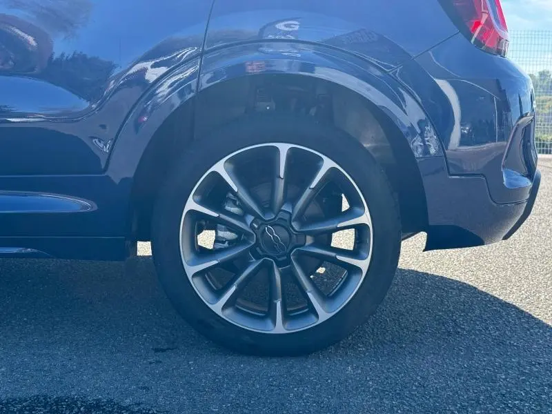 Gros plan sur la roue arrière droite d'un FIAT 500X bleu avec jante alu au design distinctif en étoile.