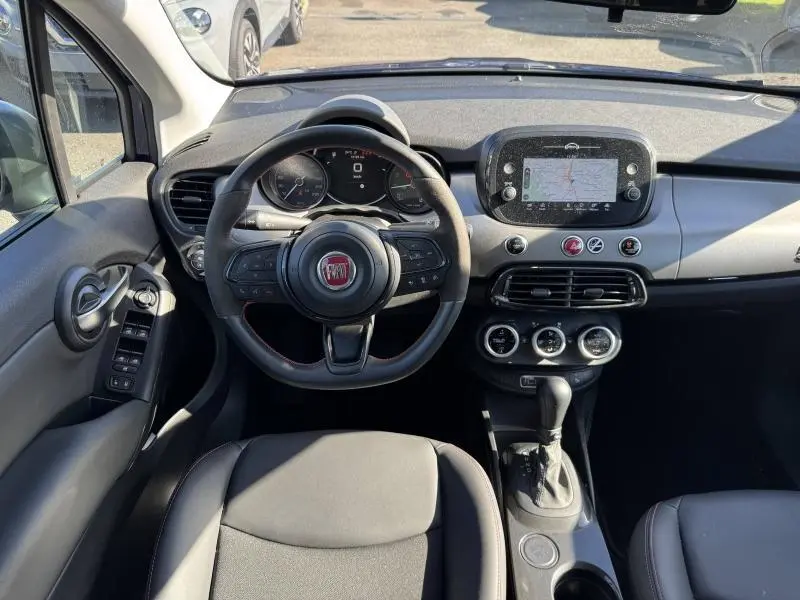 Vue intérieure avant de la Fiat 500X 2024, tableau de bord avec écran tactile GPS et volant multifonction cuir.