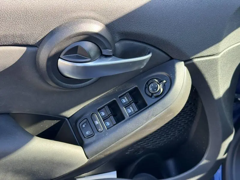 Gros plan sur la commande des vitres et la poignée intérieure côté conducteur du FIAT 500X 2024 en rouge Passione pastel.