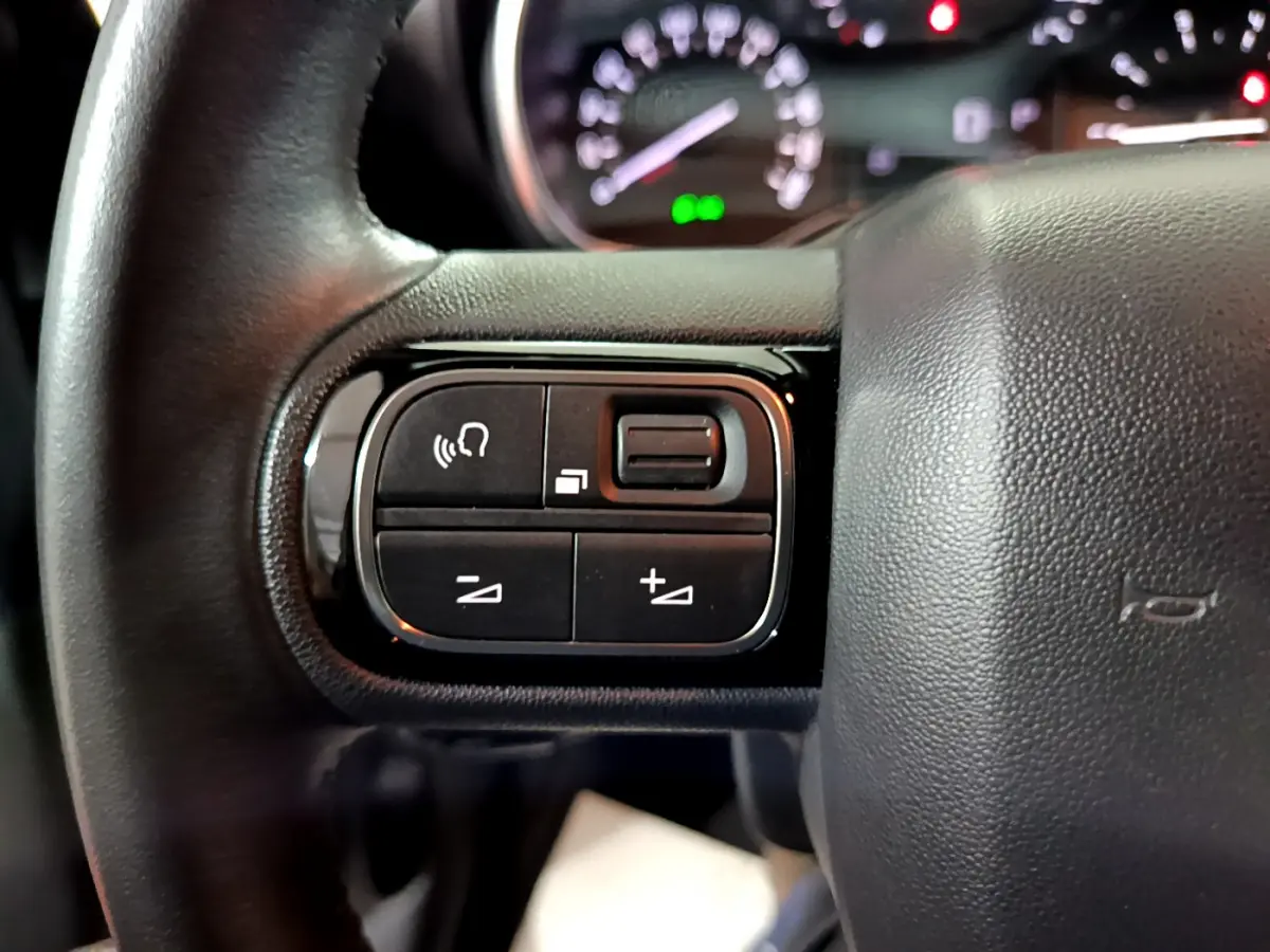 Gros plan sur les commandes gauche du volant cuir noir du Citroën C3 Aircross 2019, avec tableau de bord flou en arrière-plan.