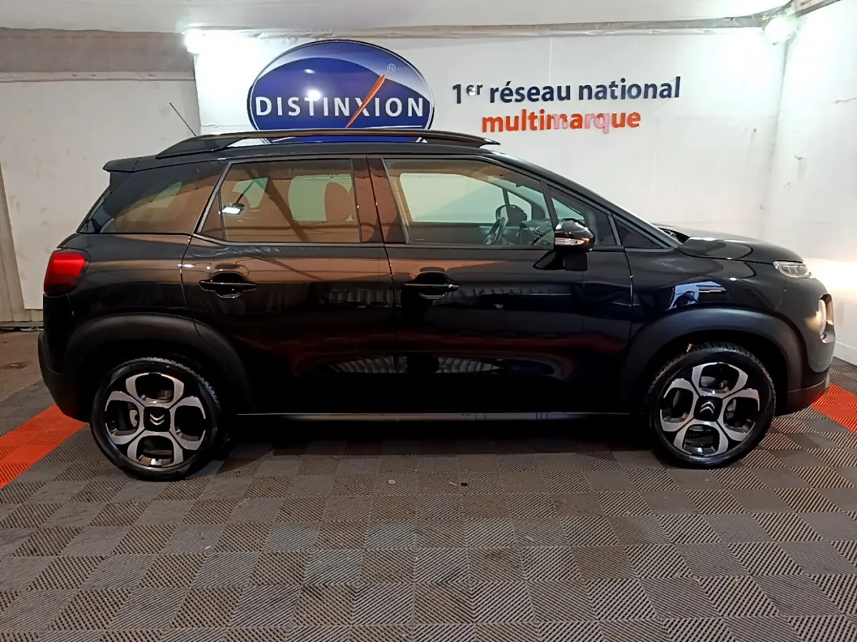 Profil côté gauche d'un Citroën C3 Aircross noir 2019 avec barres de toit et jantes distinctives en intérieur showroom.