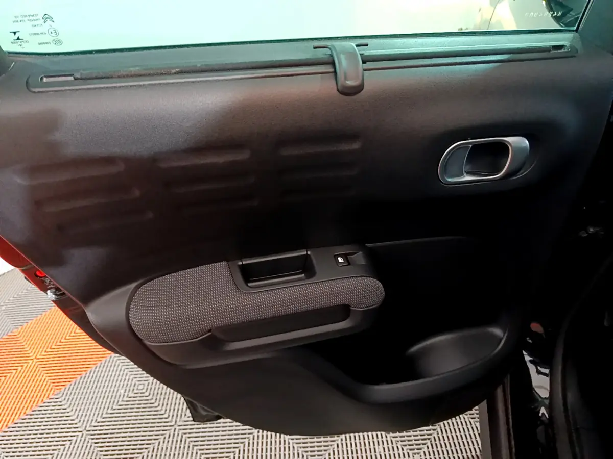 Gros plan sur la porte intérieure côté gauche du Citroën C3 Aircross noir, avec poignée argentée et accoudoir tissu.