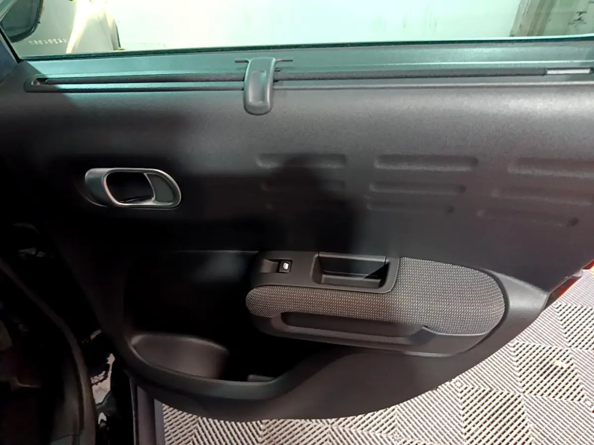 Porte intérieure côté gauche noire de la Citroën C3 Aircross PureTech 110 Shine, avec poignée et commande de vitre.