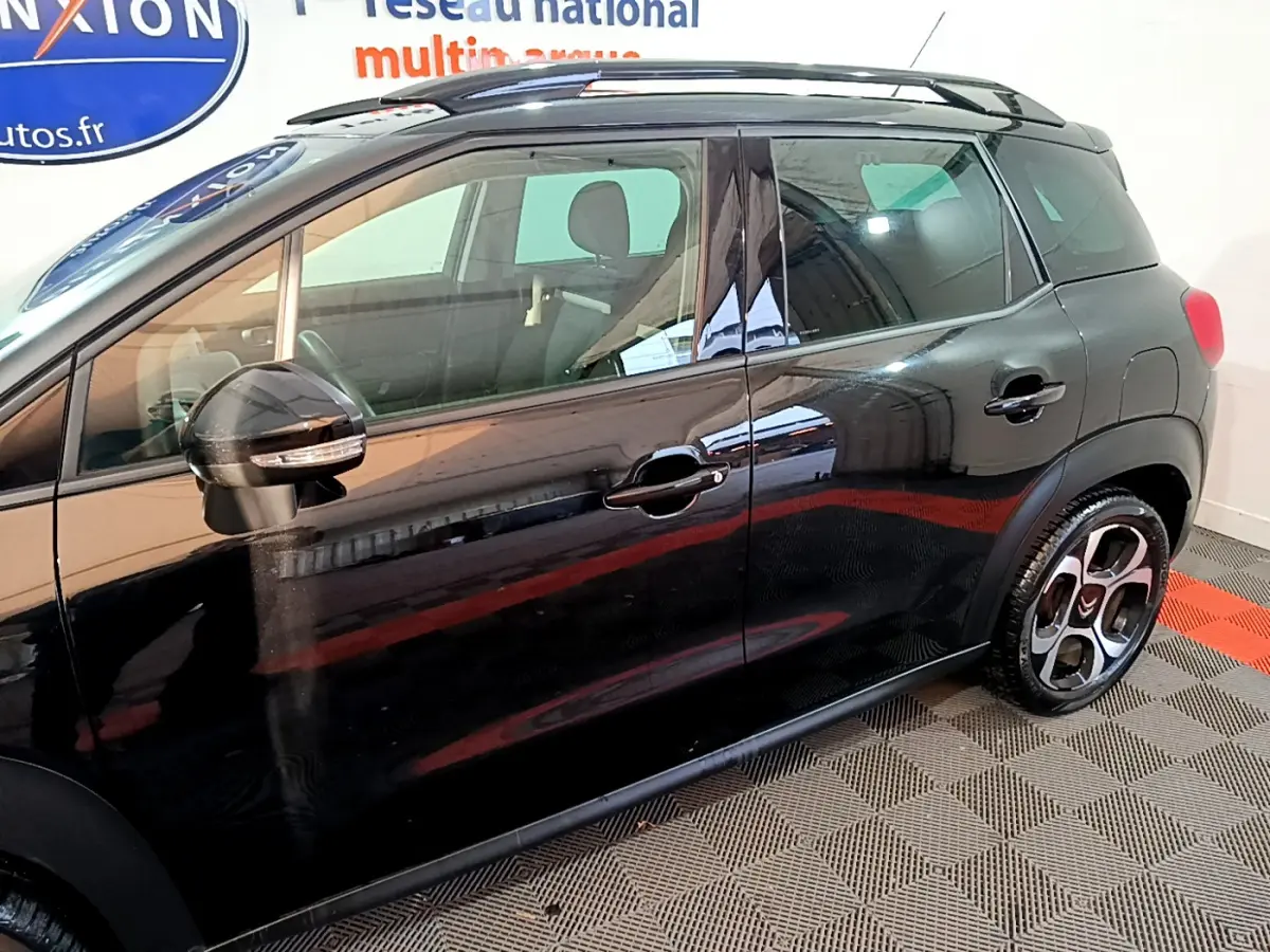 Profil côté gauche d'un Citroën C3 Aircross noir 2019 avec barres de toit et jantes distinctives en intérieur showroom.