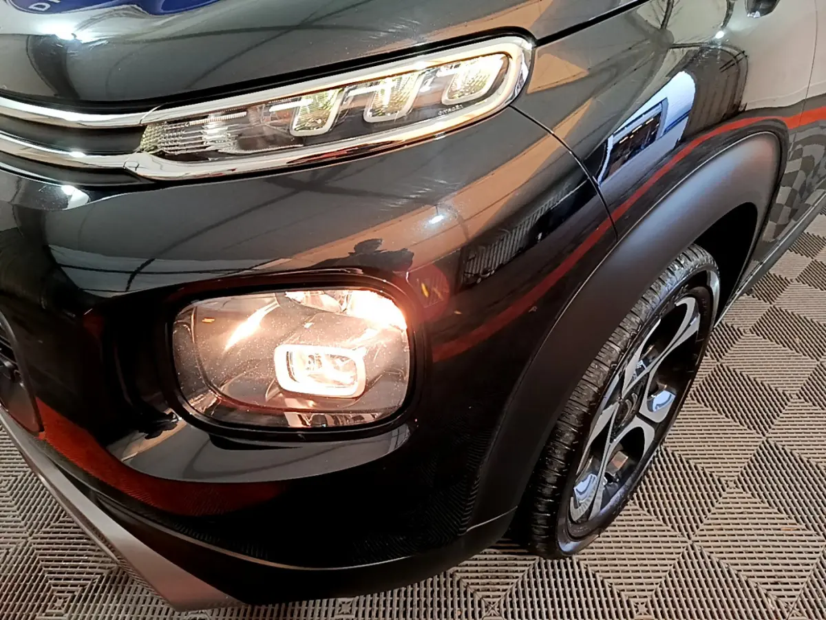 Gros plan sur le phare avant droit allumé d'un Citroën C3 Aircross noir, avec jante alliage et carrosserie brillante.