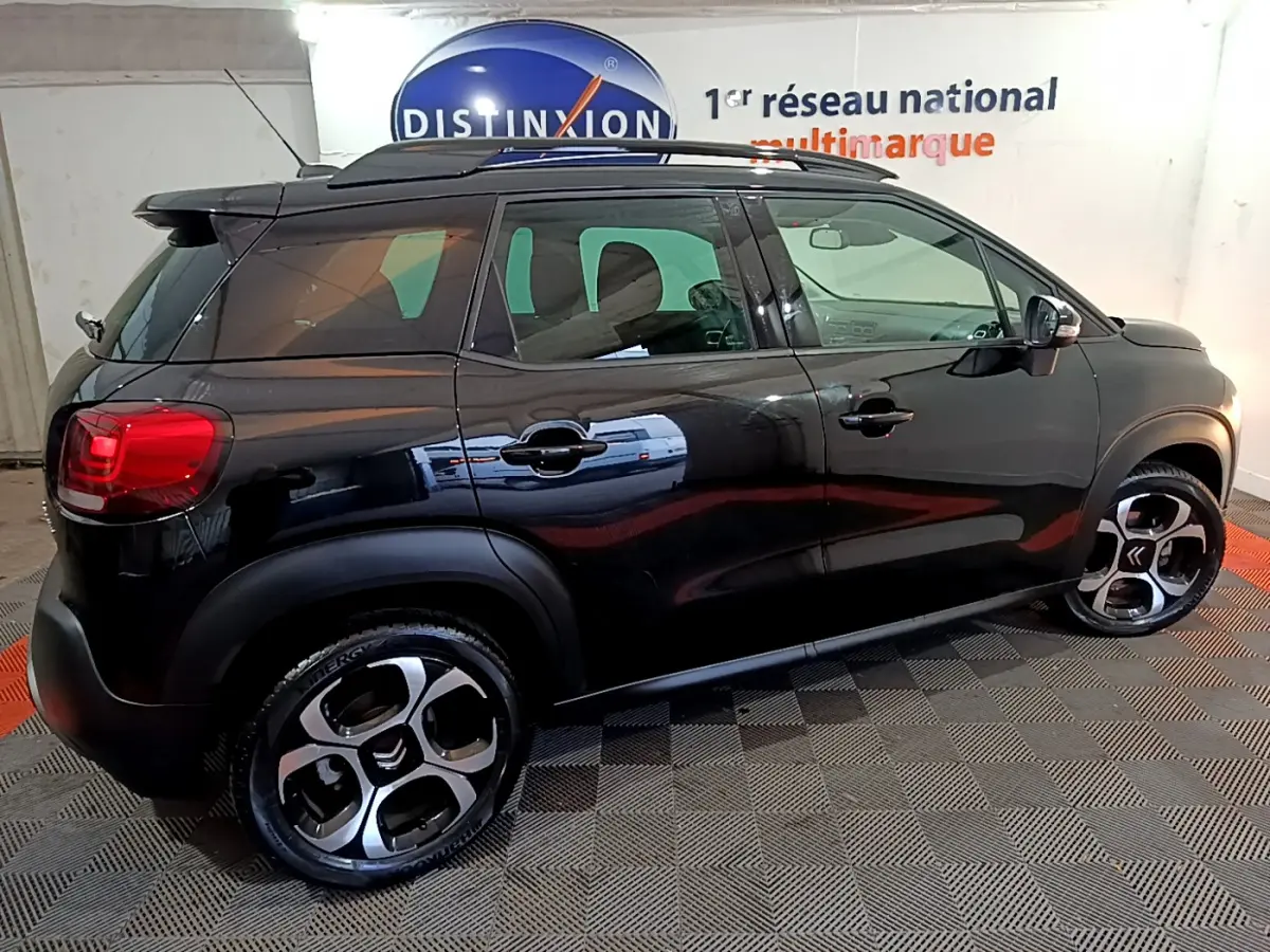 Profil côté droit d'un Citroën C3 Aircross noir 2019 avec barres de toit et jantes distinctives en intérieur showroom.