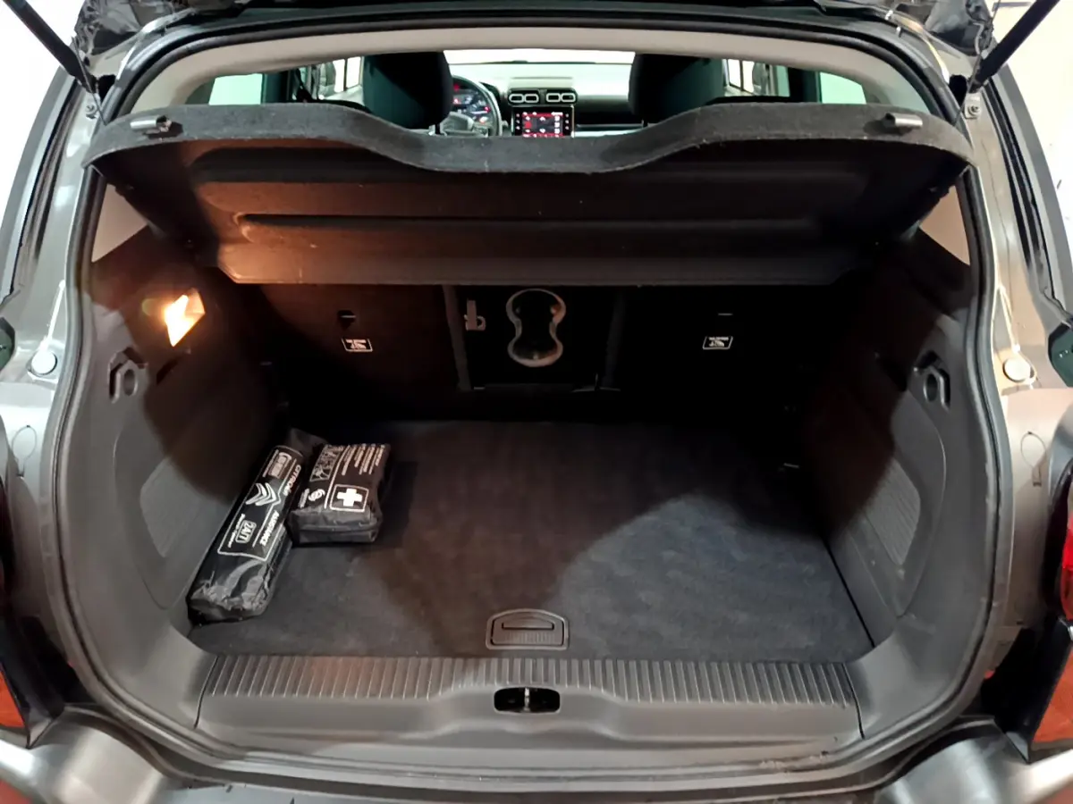 Coffre noir ouvert du Citroën C3 Aircross 2019, vue arrière avec trappe à ski et objets de sécurité posés.