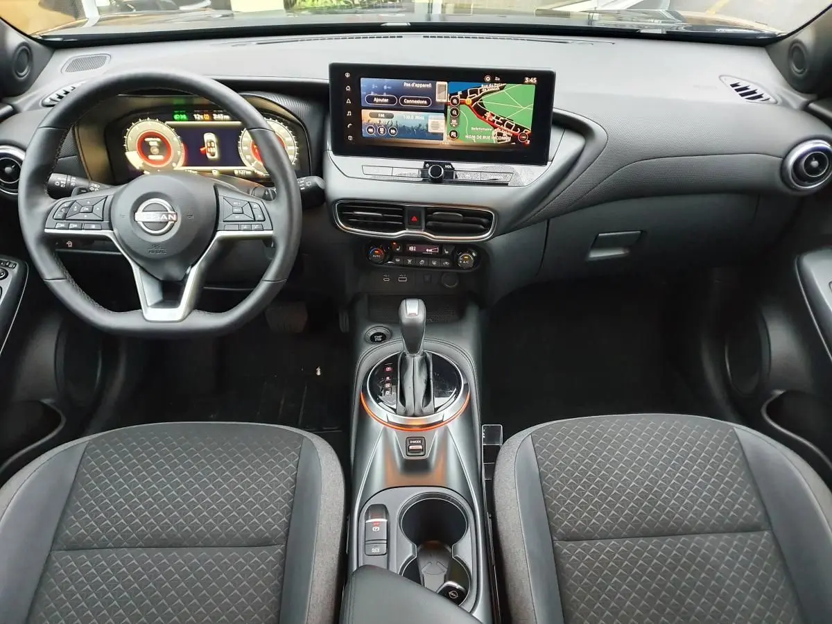 Vue intérieure avant du Nissan Juke 2025 noire, avec tableau de bord numérique et écran tactile central affichant la navigation.