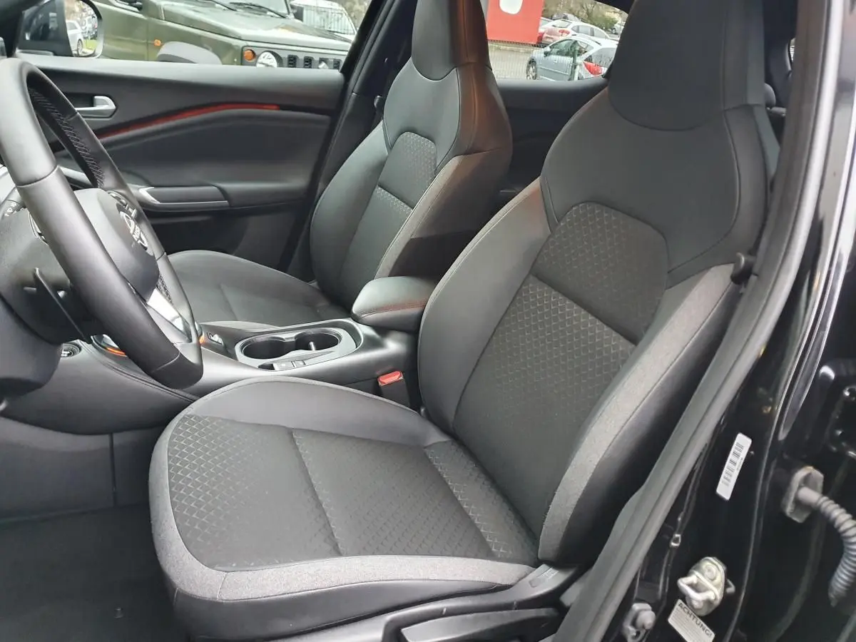 Intérieur côté conducteur du Nissan Juke noir 2025, sièges tissu gris avec console centrale et porte-gobelets visibles.