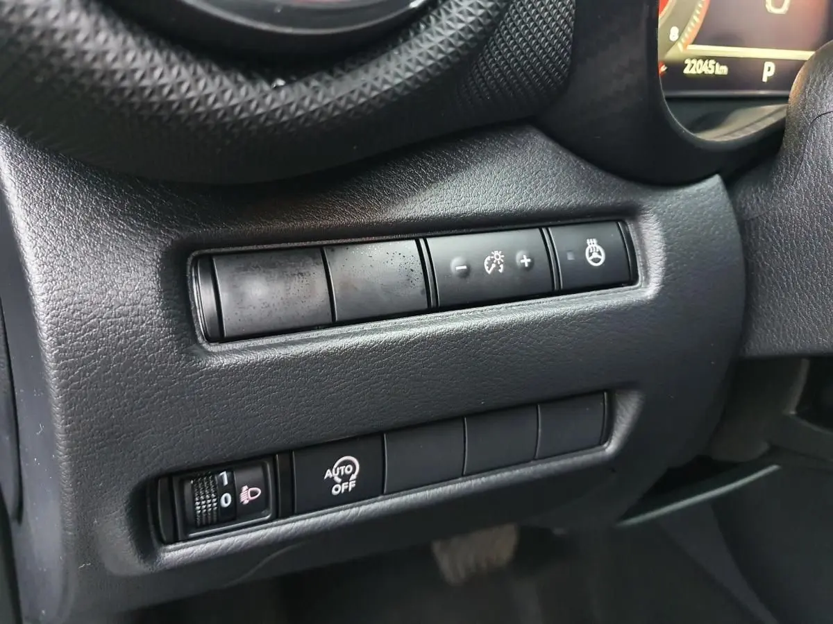 Gros plan sur les commandes de réglage d'éclairage et chauffage du volant côté gauche du tableau de bord du Nissan Juke noir 2025.