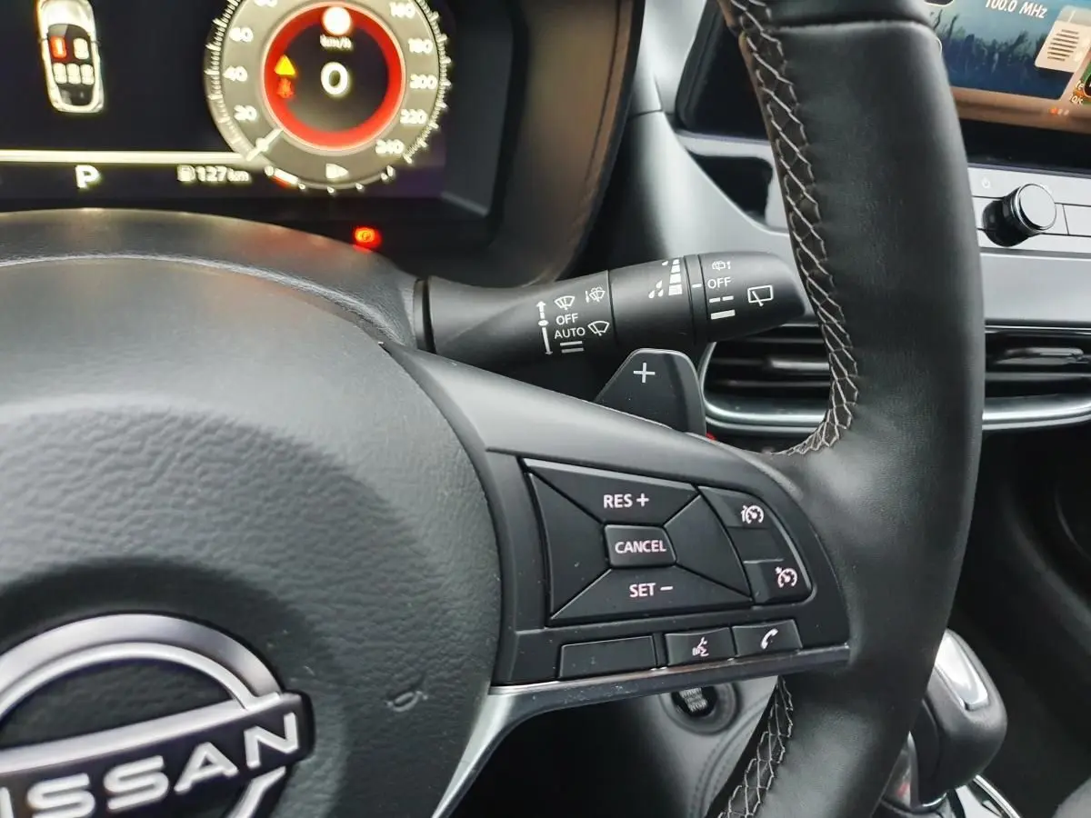 Gros plan sur le volant cuir noir du Nissan Juke 2025 avec commandes de régulateur et tableau de bord numérique.