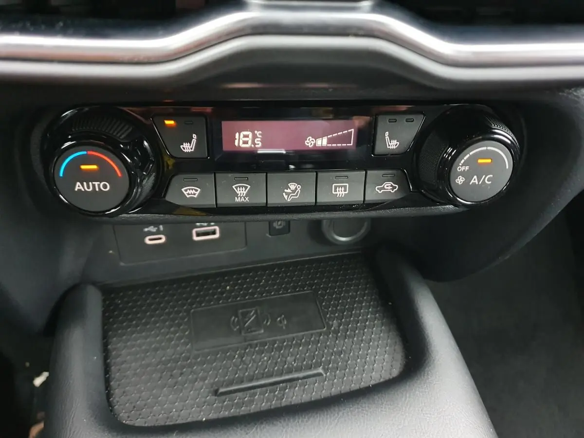 Vue rapprochée de la console centrale du Nissan Juke noire 2025, mettant en valeur la climatisation automatique et le chargeur sans fil.
