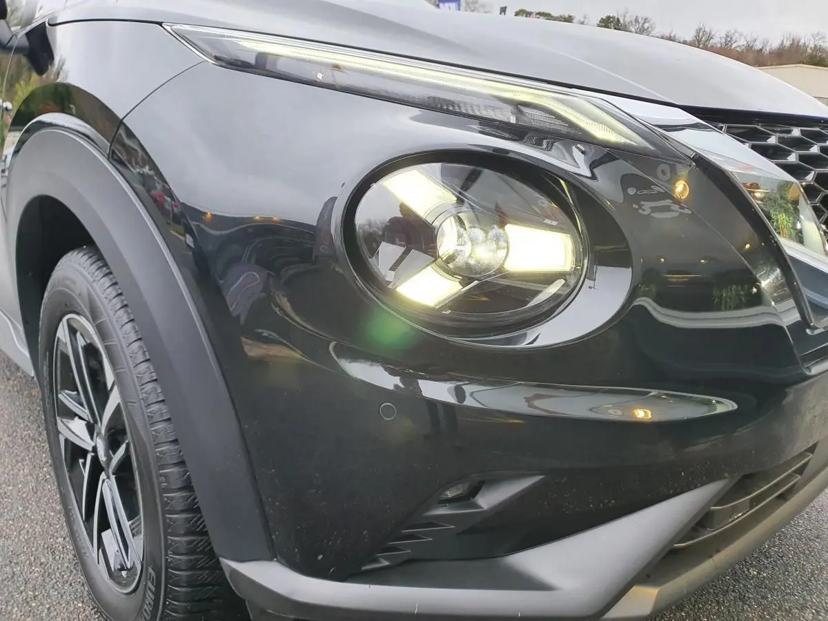 Gros plan sur l'avant droit noir métallisé du Nissan Juke 2025 avec phare allumé et jante alliage 17 pouces.