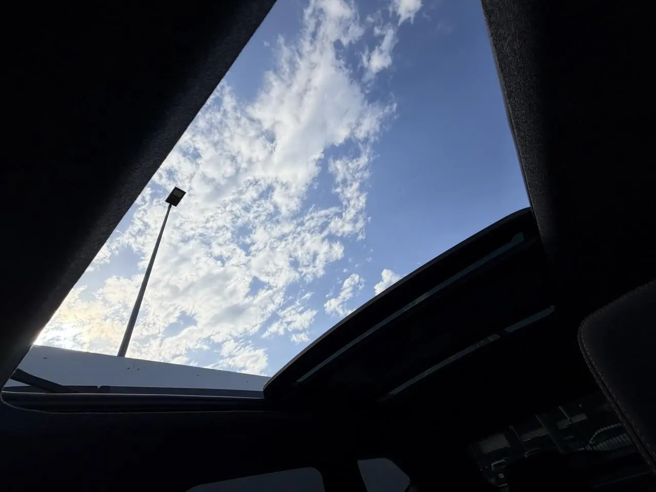 Vue intérieure du toit ouvrant panoramique ouvert du Dacia Bigster noir, avec ciel bleu et nuages visibles.