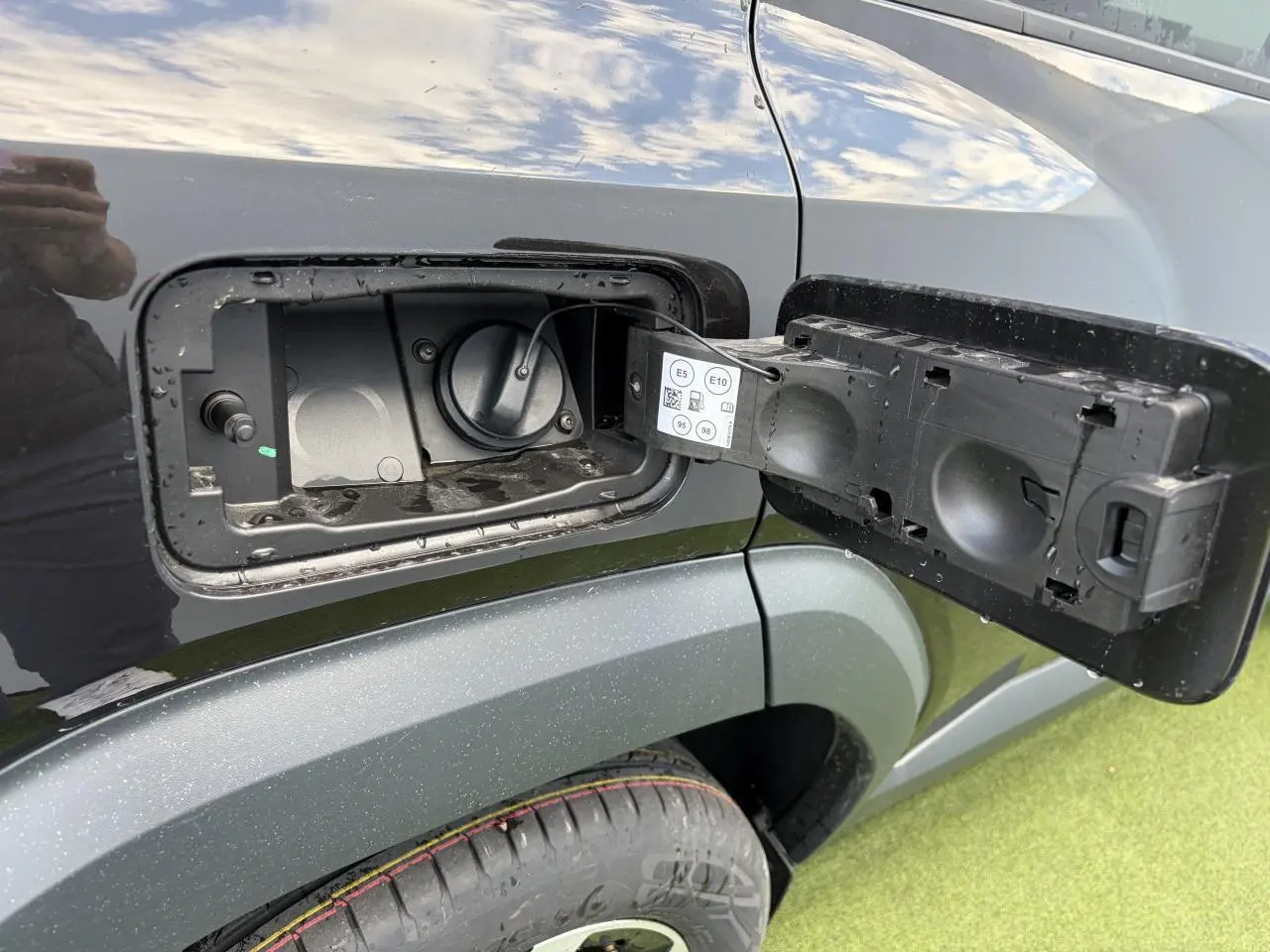 Gros plan sur la trappe de carburant ouverte côté gauche du Dacia Bigster noir nacré avec jante 18 pouces visible.