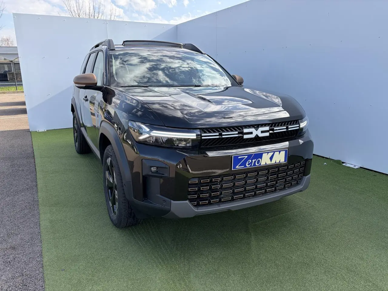 Vue 3/4 avant du Dacia Bigster noir nacré avec calandre brun cuivré et toit panoramique ouvrant.