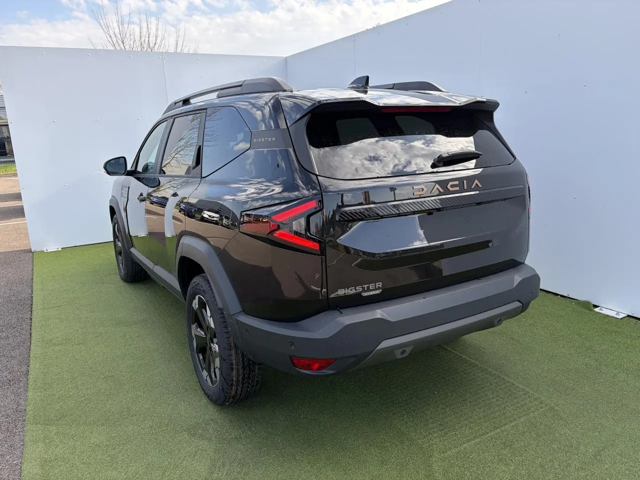 Vue 3/4 arrière gauche du Dacia Bigster noir nacré avec signature lumineuse LED et barres de toit noires.