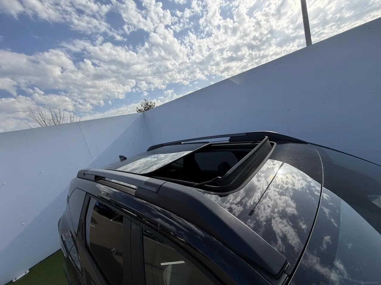 Toit ouvrant panoramique ouvert sur le côté gauche d’un Dacia Bigster noir nacré avec barres de toit noires.