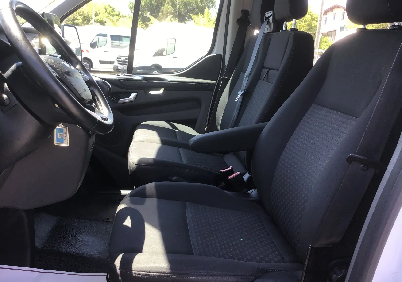 Vue intérieure côté conducteur du Ford Transit Custom Kombi 2023, sièges noirs et volant multifonction visibles.