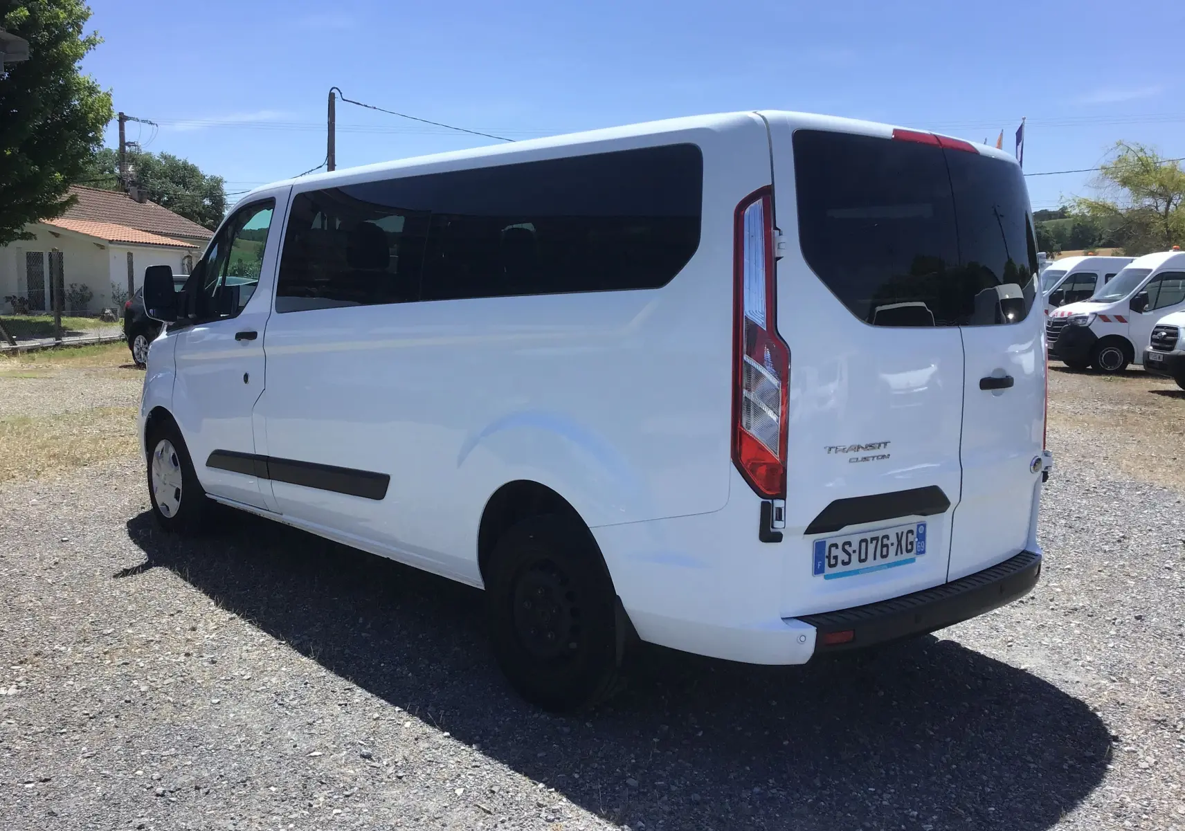 Vue 3/4 arrière droite d’un Ford Transit Custom Kombi blanc, avec vitres arrière teintées et hayon fermé.
