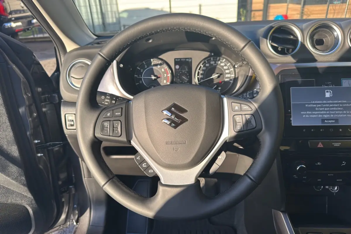 Vue intérieure centrée sur le volant cuir noir du Suzuki Vitara 2025, avec tableau de bord et écran multimédia visible.
