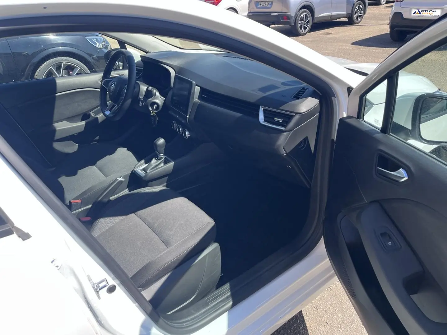 Vue intérieure côté conducteur de la Renault Clio blanc Quartz, montrant sièges noirs et tableau de bord moderne.
