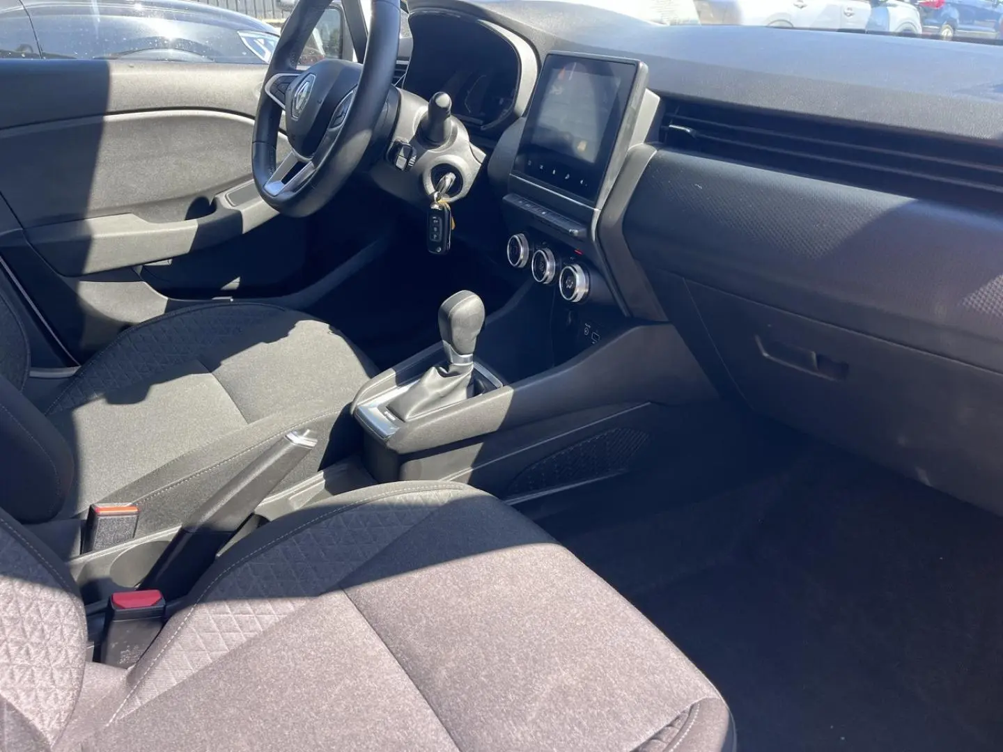 Intérieur avant droit de la Renault Clio blanc Quartz 2021, montrant sièges noirs et console centrale avec écran tactile.