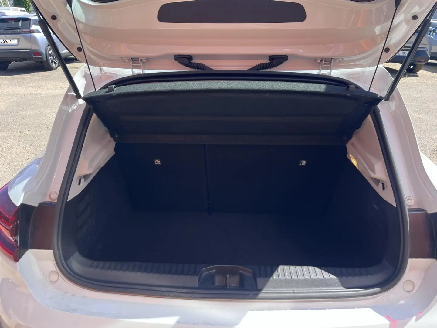 Coffre ouvert vu de l'arrière d'une Renault Clio blanc Quartz, espace de chargement vide et propre.