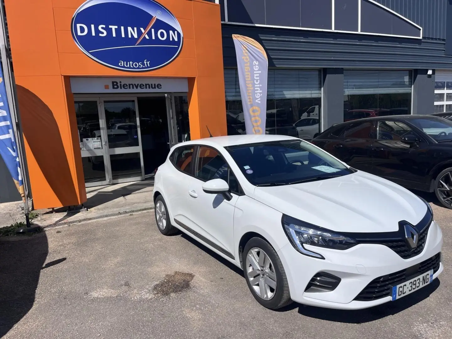 Renault Clio 1.6 E-Tech blanc Quartz vue 3/4 avant droit devant un garage avec enseigne orange.