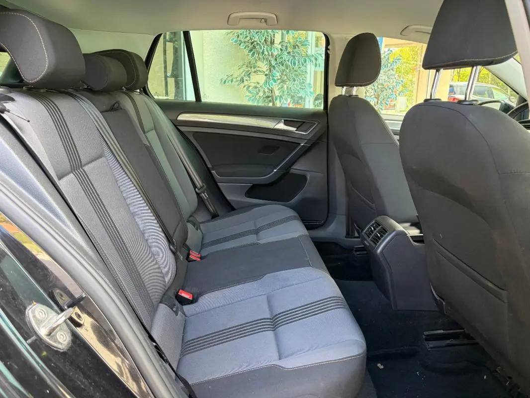 Vue intérieure côté gauche des sièges arrière d'une Volkswagen Golf 7 noire, tissu gris à rayures, avec porte ouverte.
