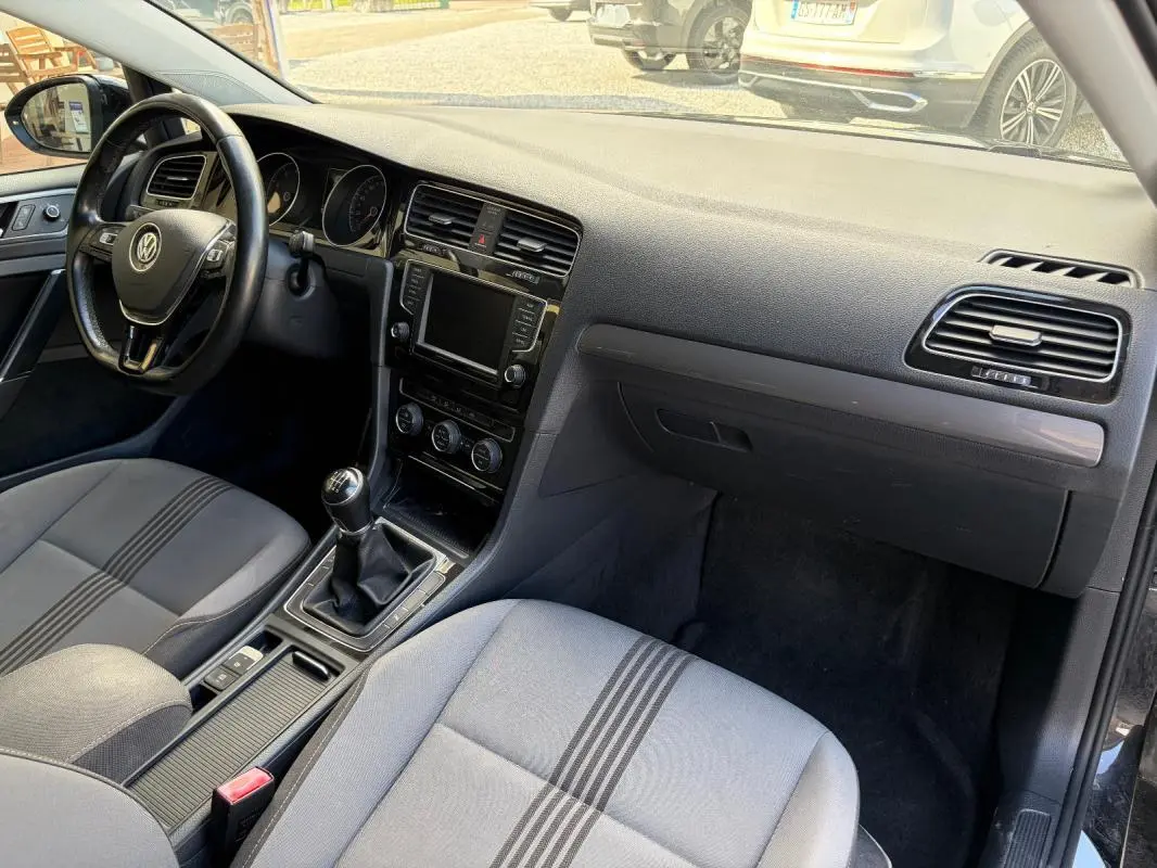 Vue intérieure côté conducteur de la Volkswagen Golf 7 noire, volant cuir multifonctions et boîte manuelle visibles.