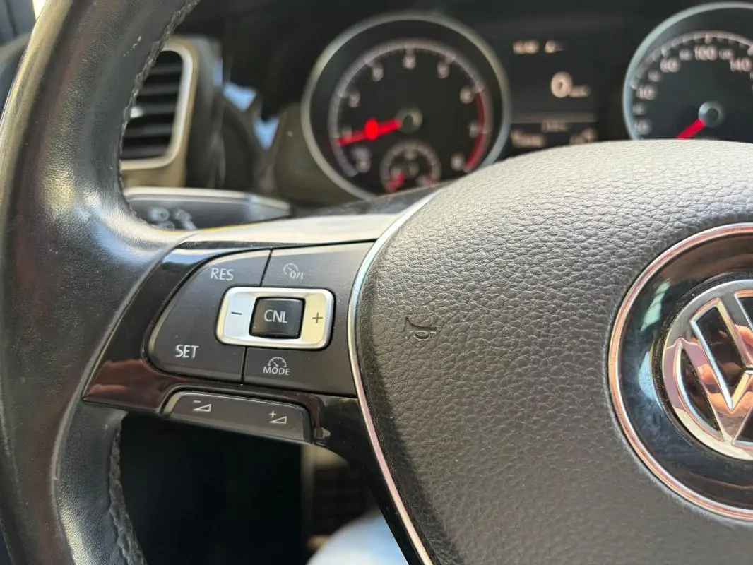 Gros plan sur le volant cuir noir multifonctions d’une Volkswagen Golf 7 avec commandes de régulateur de vitesse.