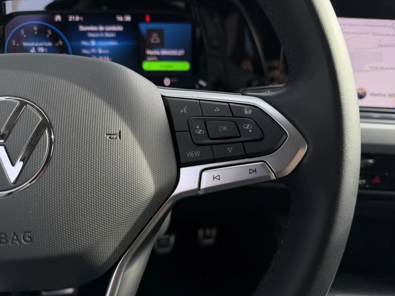 Gros plan sur le volant multifonction cuir de la Volkswagen Golf 8 gris lunaire avec commandes et affichage numérique en arrière-plan.