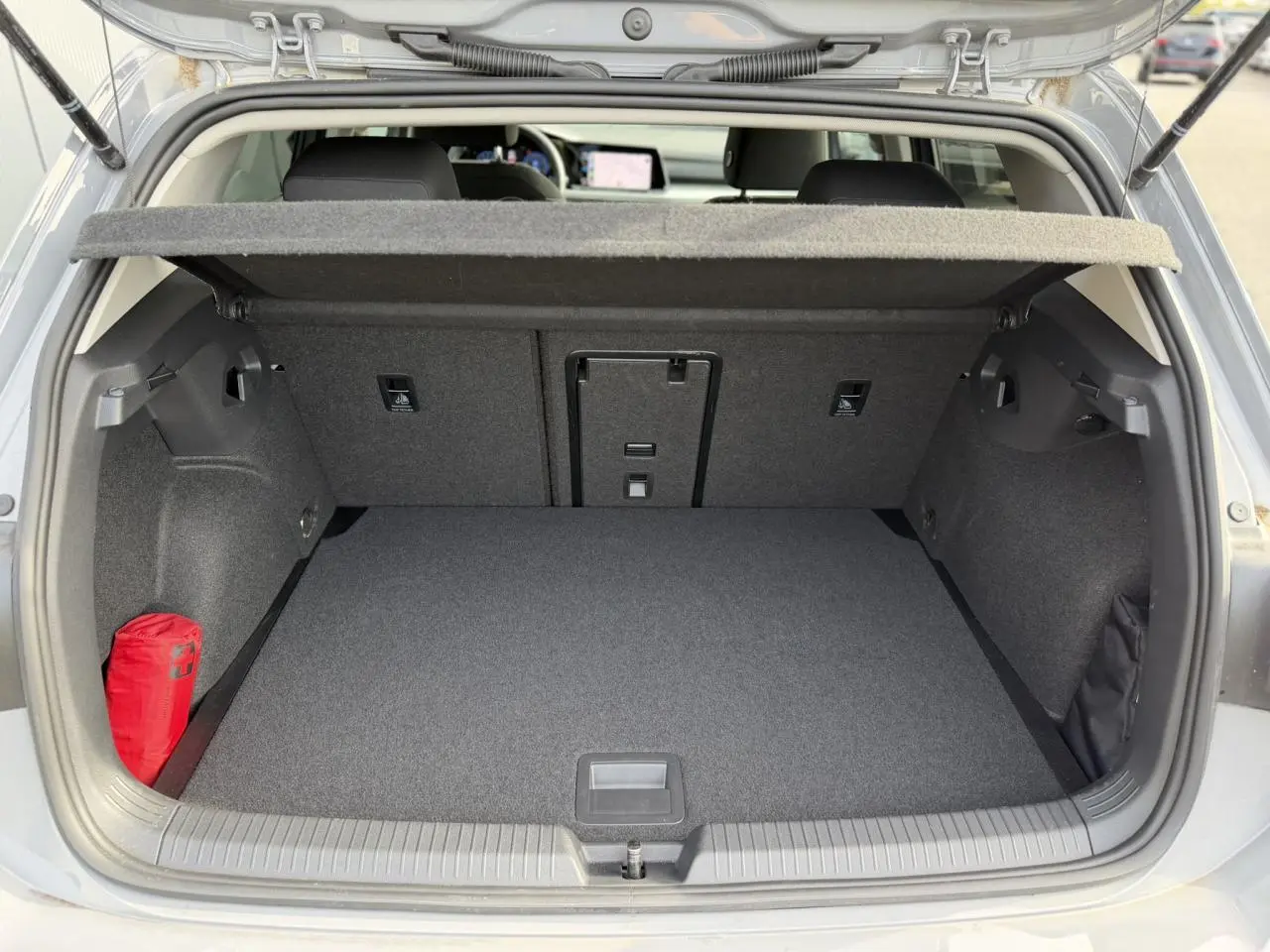 Coffre ouvert d'une Volkswagen Golf 8 gris lunaire, montrant un espace de rangement propre avec trappe centrale et kit de secours rouge.