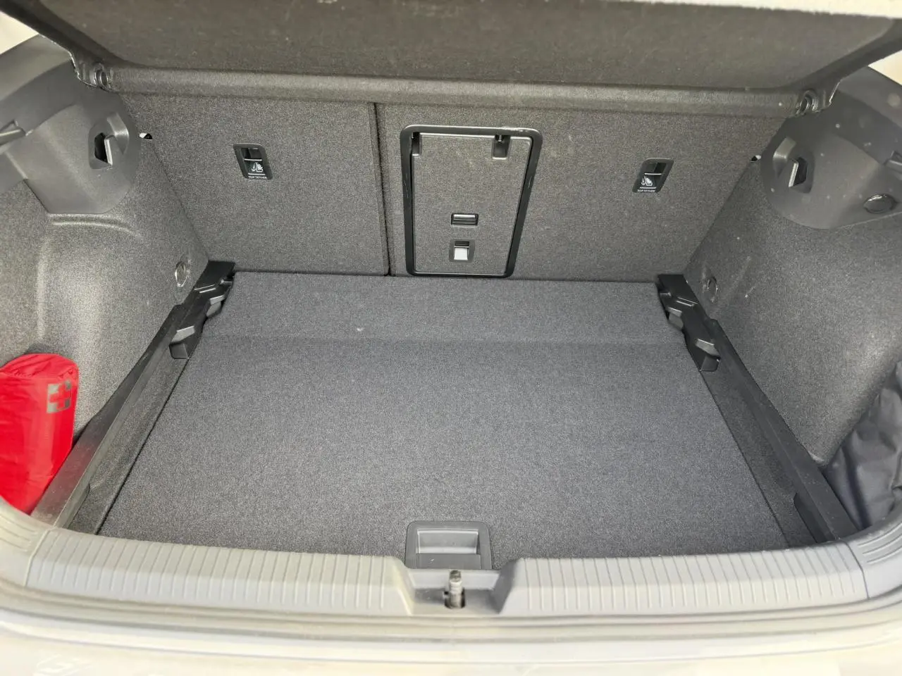 Coffre ouvert vu de face de la Volkswagen Golf 8 gris lunaire, avec tapis et rangement intérieur visible.