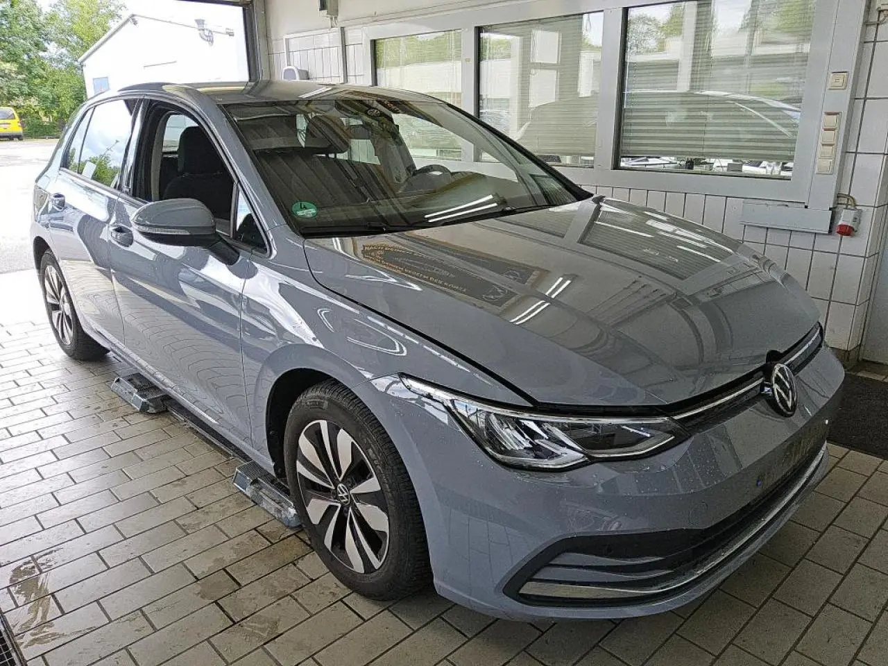 Volkswagen Golf 8 gris lunaire vue 3/4 avant droit dans un garage avec jantes alliage et phares LED.