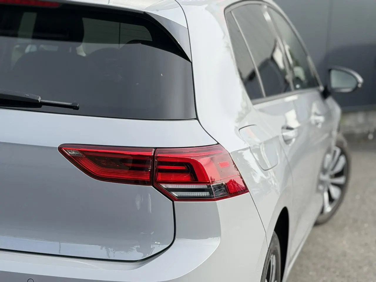 Vue arrière droite d'une Volkswagen Golf 8 gris lunaire avec feux arrière LED et jantes alliage visibles.