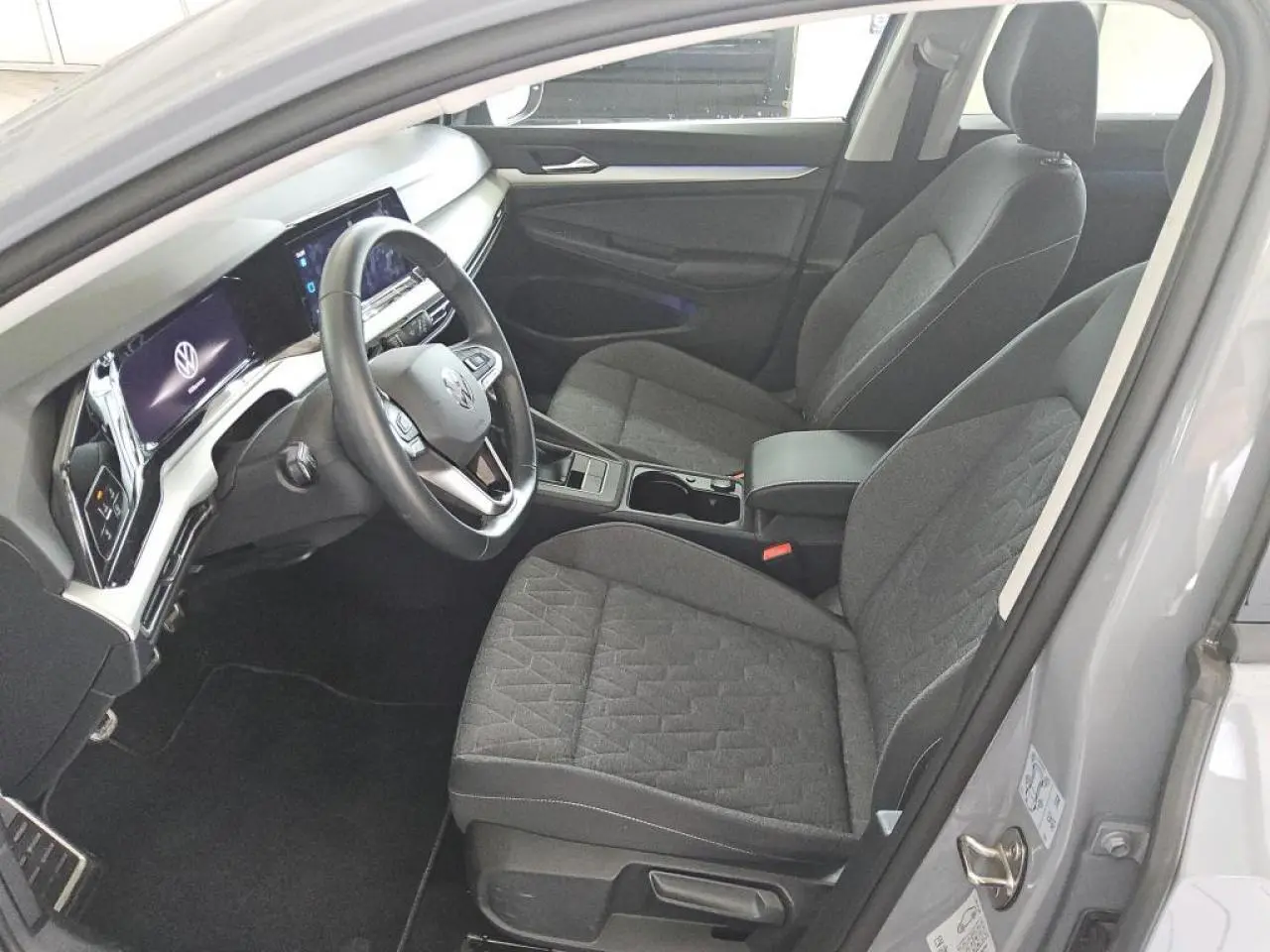 Intérieur avant droit de la Volkswagen Golf 8 gris lunaire, sièges tissu et tableau de bord digital moderne.