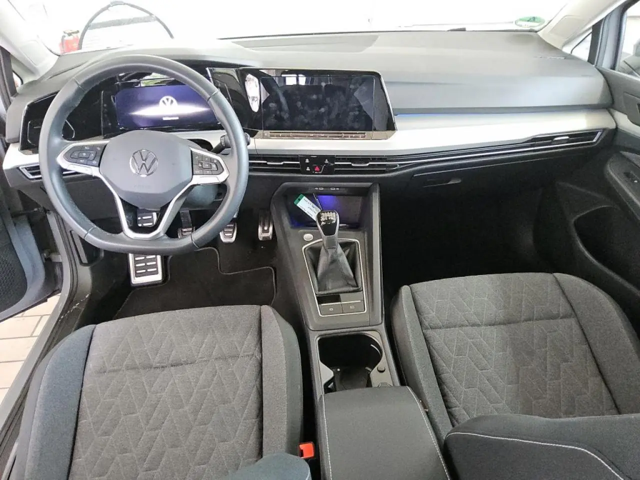 Vue intérieure frontale de la Volkswagen Golf 8 avec tableau de bord digital et volant multifonction en cuir noir.