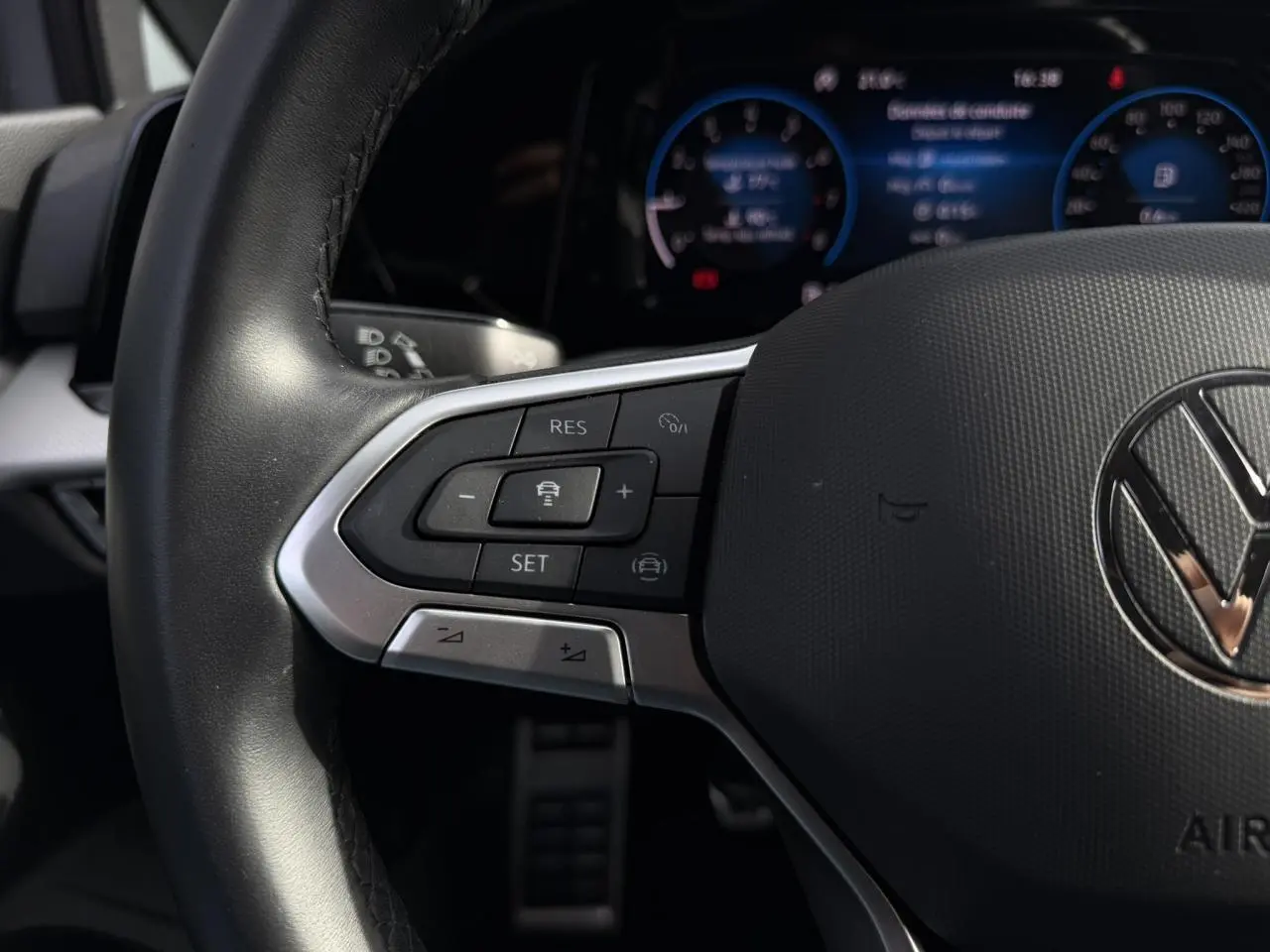 Gros plan sur le volant multifonction cuir de la Volkswagen Golf 8 gris lunaire, avec commandes de régulateur et tableau de bord numérique flou.