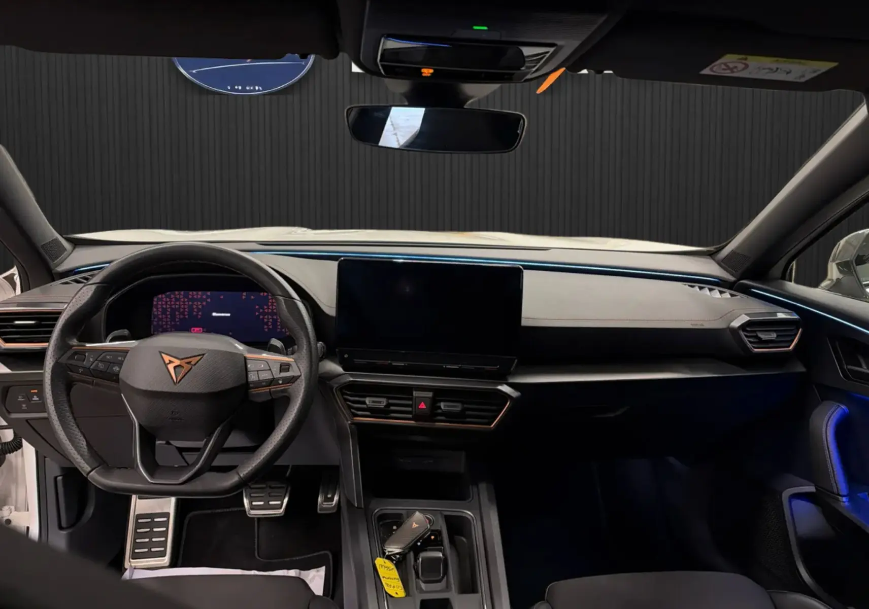 Vue intérieure avant du tableau de bord noir du CUPRA Formentor blanc 2024 avec écran tactile central et volant multifonction.