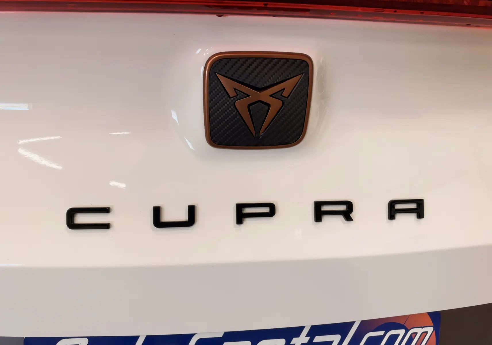 Gros plan sur le logo CUPRA noir et cuivre sur fond blanc à l'arrière du véhicule.