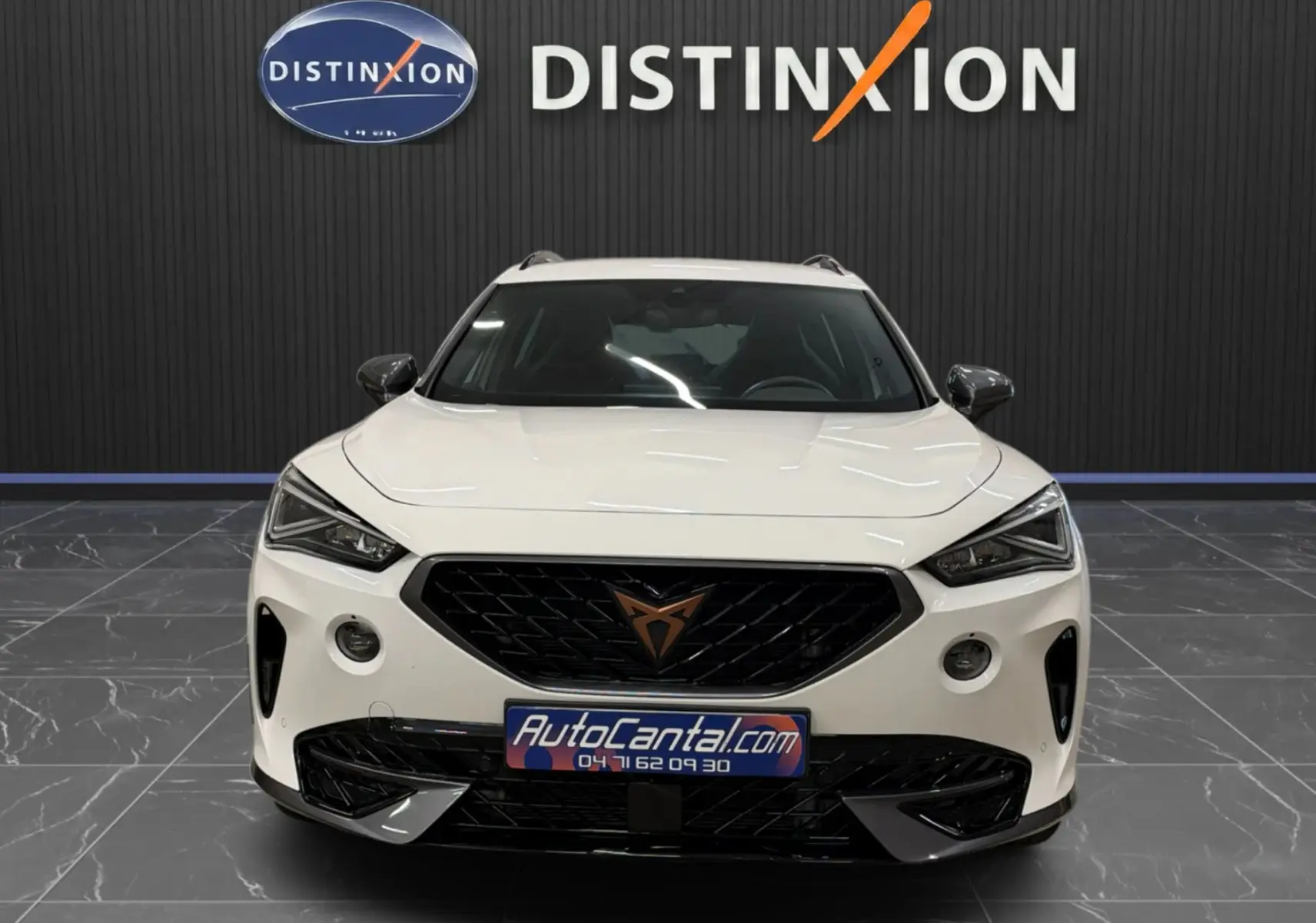 Vue frontale d'un CUPRA Formentor blanc 2024 avec calandre noire et logo cuivre, dans un showroom intérieur.