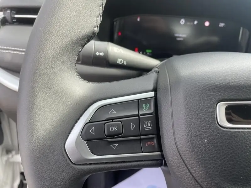 Gros plan sur les commandes au volant gauche du Jeep Compass blanc 2024, version hybride essence avec boutons de navigation et appels.