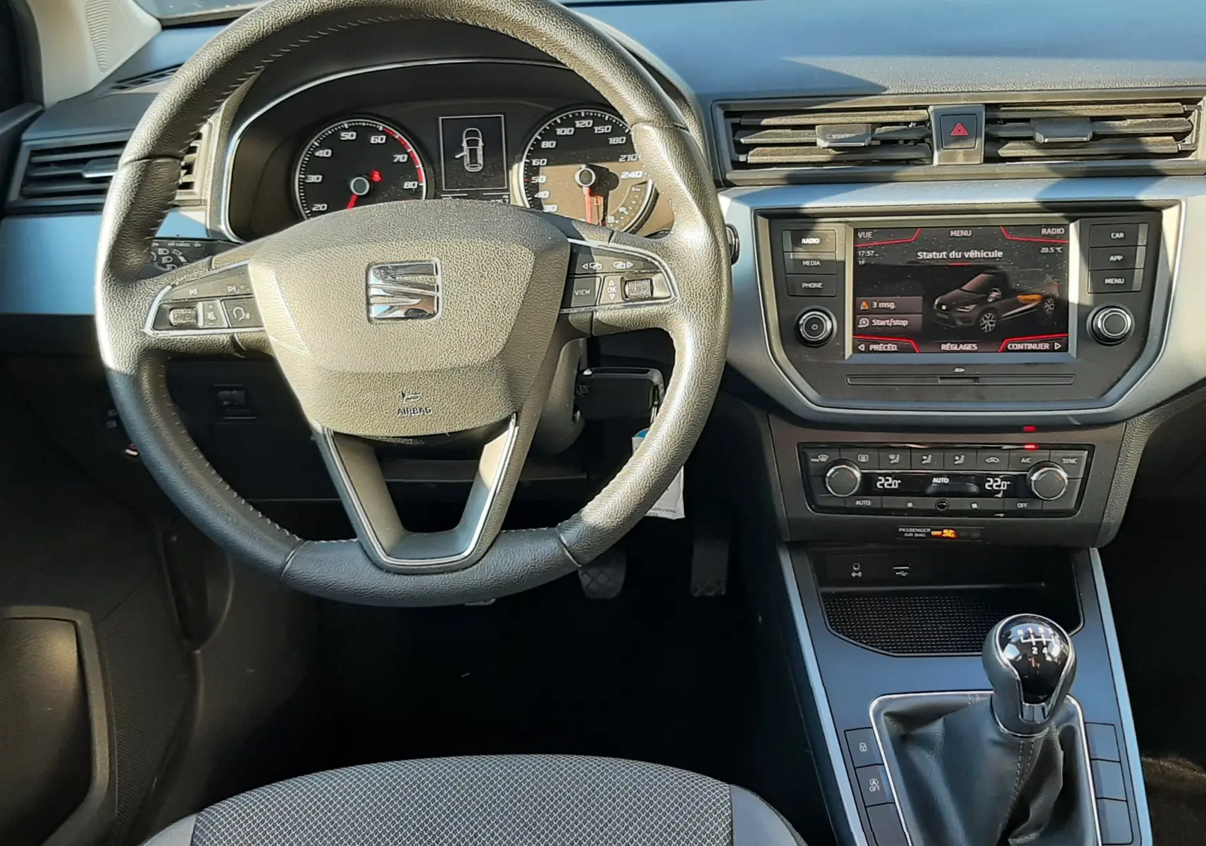 Vue intérieure frontale du tableau de bord et volant du SEAT Arona gris magnetic, avec levier de vitesse manuel et écran tactile.