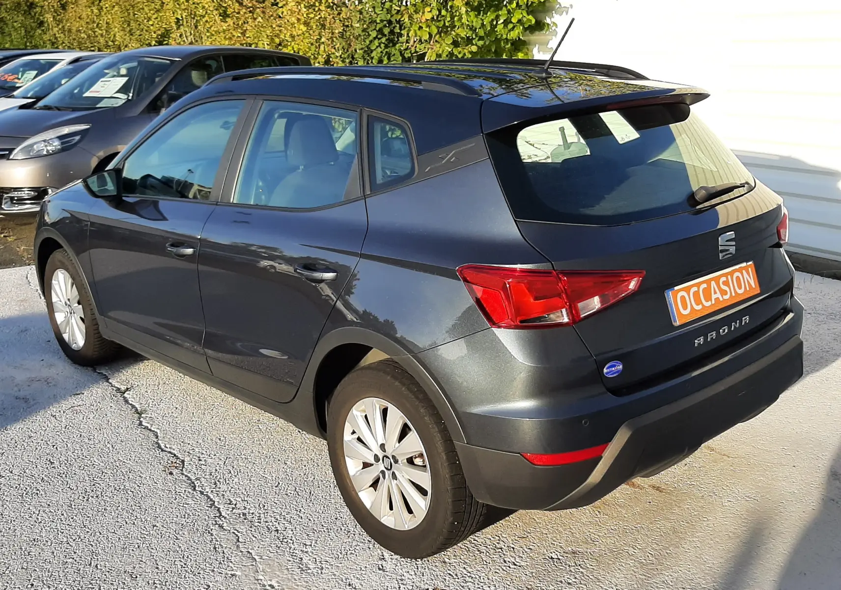 Vue 3/4 arrière droite d'une SEAT Arona gris magnetic avec toit noir, en stationnement extérieur au soleil.