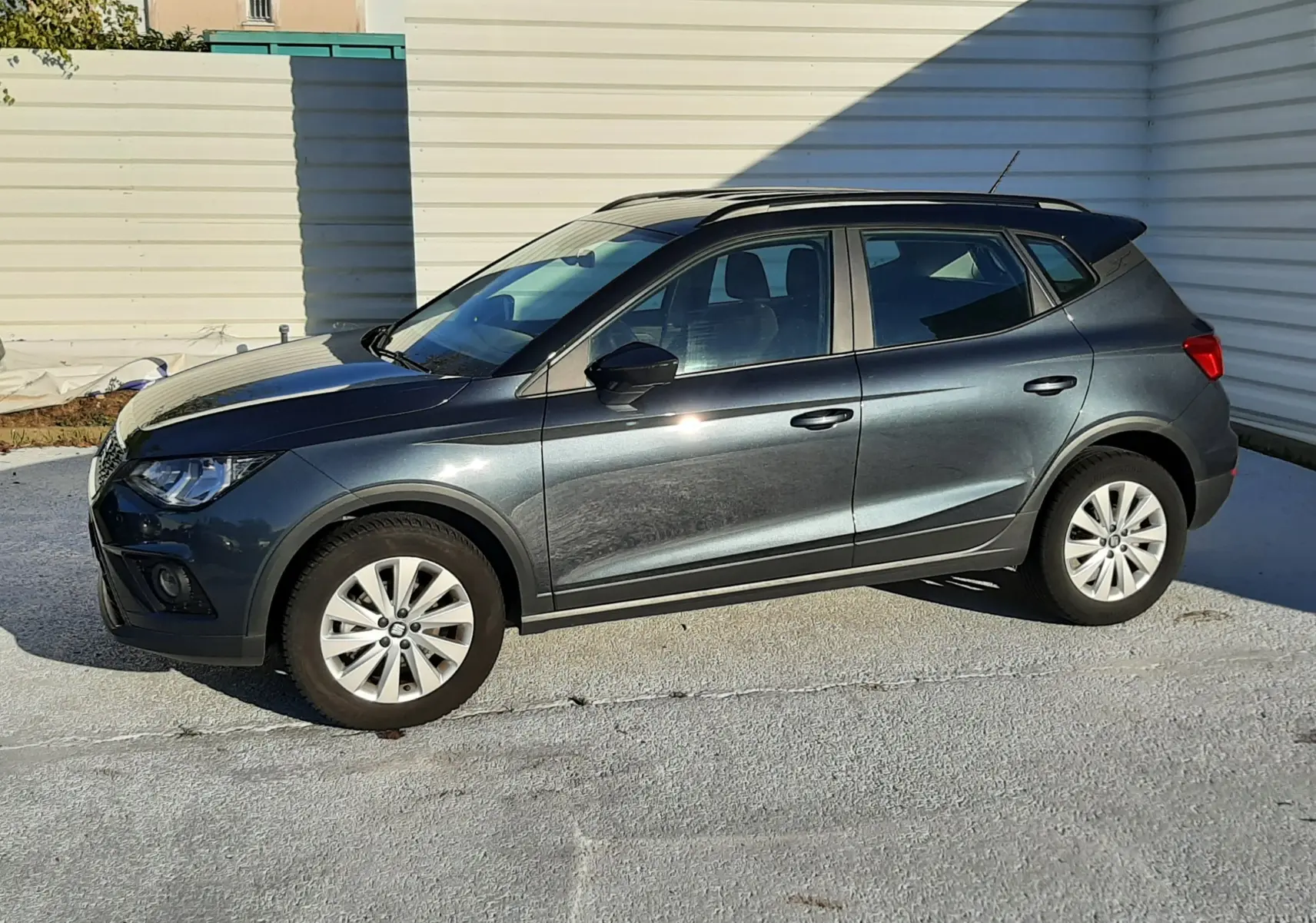 SEAT Arona gris magnetic avec toit noir, vue de profil côté gauche sur fond urbain lumineux.